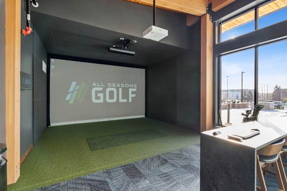 A room with a green carpet and a screen displaying "All Seasons GOLF".