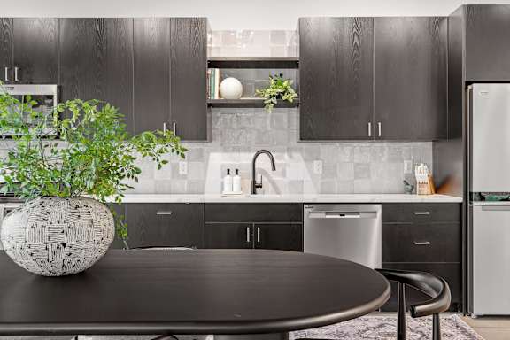 A modern kitchen with black cabinets and a round table with a plant on it.
