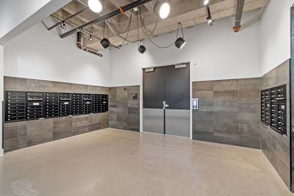 A room with a concrete floor and walls, a black door, and a white ceiling with lights.