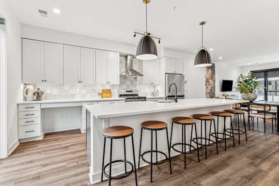 A kitchen with white cabinets and a white island with four stools.