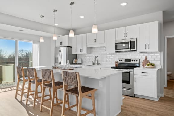 a kitchen with white cabinets and a white island with chairs