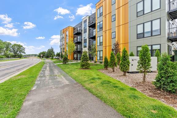 A long concrete pathway leads to a row of modern apartment buildings.
