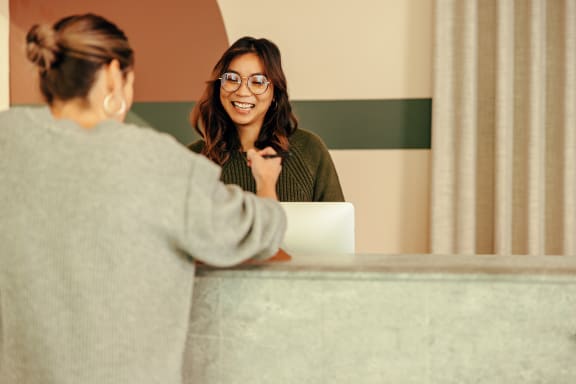 two women talking at a hotel desk with a laptop