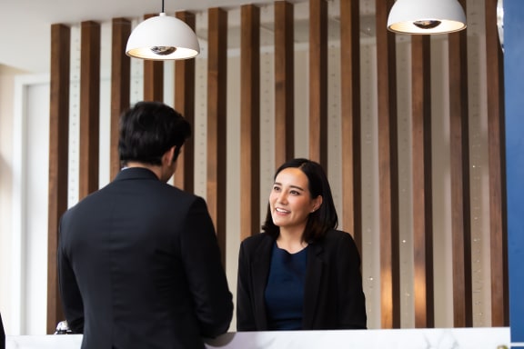 a woman smiling at a counter while talking to a man in front of a mirror