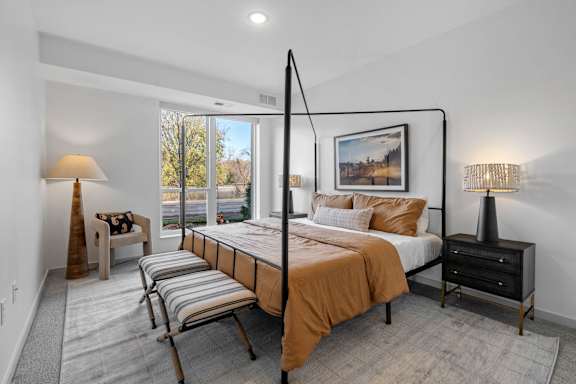 A bedroom with a large bed and a chair by the window.