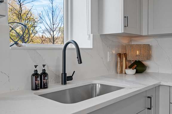 A modern kitchen with a stainless steel sink and white countertop.