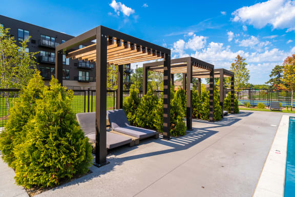 a pergola with lounge chairs on a patio next to a pool