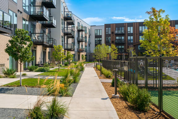 a pathway lined with trees and plants in front of an apartment complex
