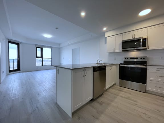 Bayfield Tower Apartments 3 bedroom 2 bathroom variation A kitchen with stainless steel appliances and white cabinets and open to living room with large window and glass patio door