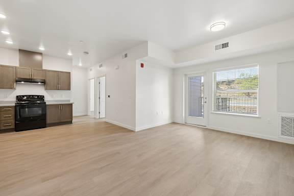 A spacious room with wooden flooring and a kitchen area with a stove and cabinets.