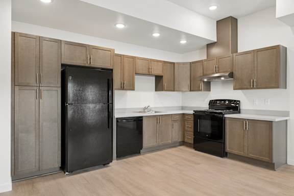 A black fridge and oven in a kitchen with wooden floors and brown cabinets.