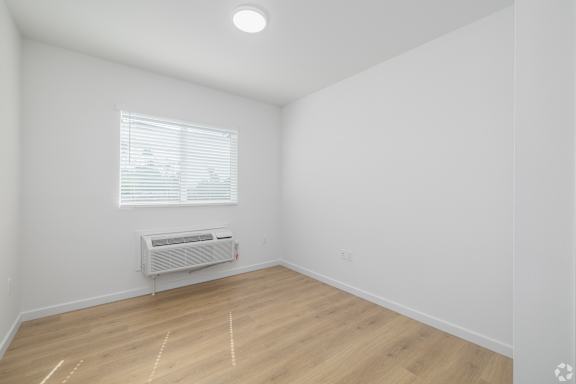 A room with a window and a white air conditioner on the wall.
