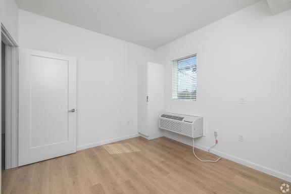 A room with a door, a window with blinds, and a wall-mounted air conditioner unit.