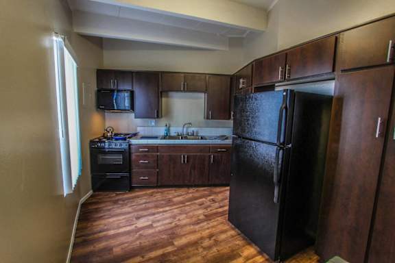 a kitchen with dark wood cabinets and a black refrigerator&#xA0;at The Marquee Apartments, North Hollywood, CA 91605