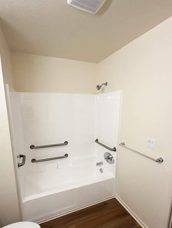 A white bathtub with silver grab bars in a small bathroom.