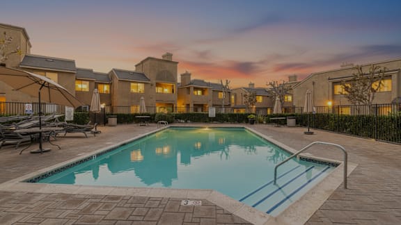 A swimming pool in front of a building with a sunset in the background.