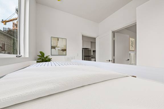 A white bed with a white mattress is in the foreground of a room with white walls.