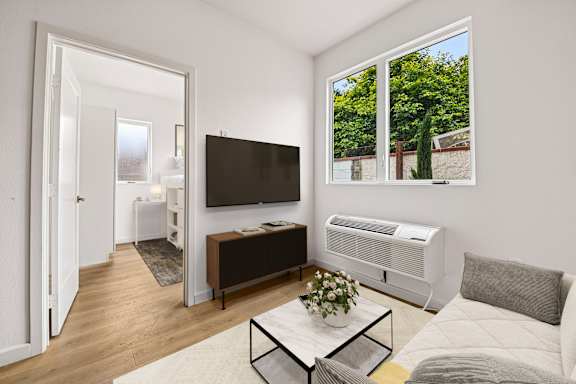A living room with a white sofa, a black TV, and a glass coffee table.