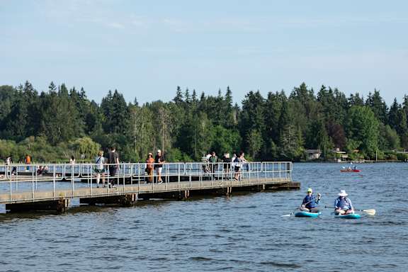 People are kayaking on a lake with a dock in the background.
