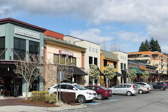 A row of parked cars in front of a row of shops.