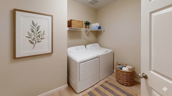 A laundry room with a washer and dryer, a basket, and a framed leaf picture on the wall.
