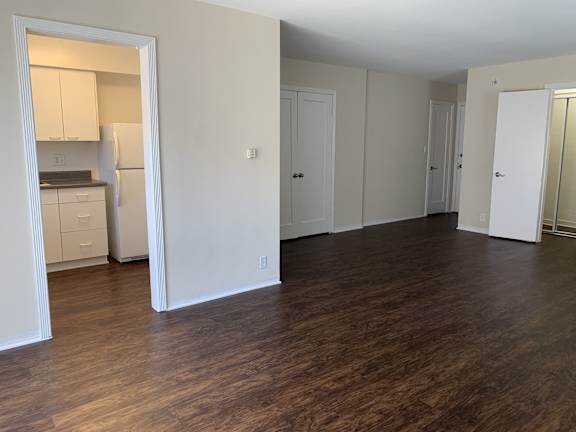 A kitchen with white cabinets and a white refrigerator is visible through an open door.