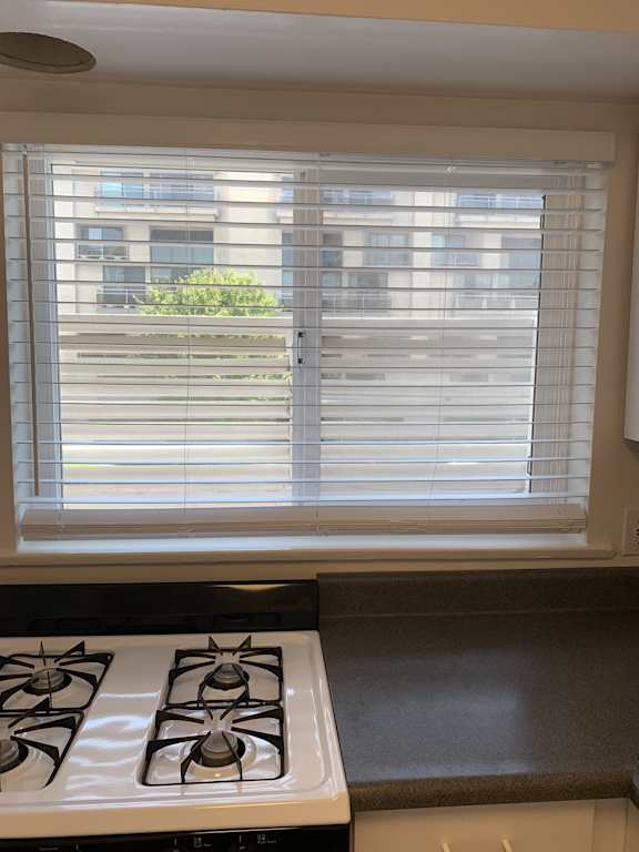 A kitchen with a stove top oven and a window with blinds.