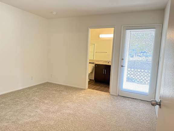 A room with a carpeted floor and a door leading to a balcony.