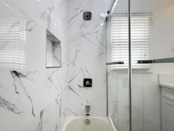 A white bathroom with a marble wall and a glass shower door.