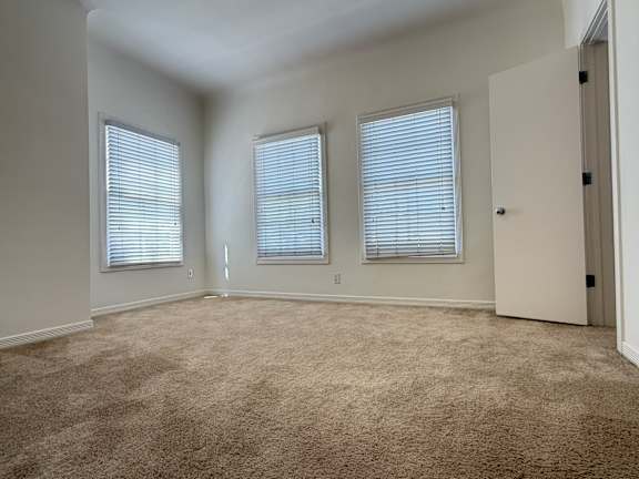 A room with carpeted floor and three windows.