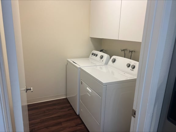 a washer and dryer in a room with a wooden floor and white cabinets