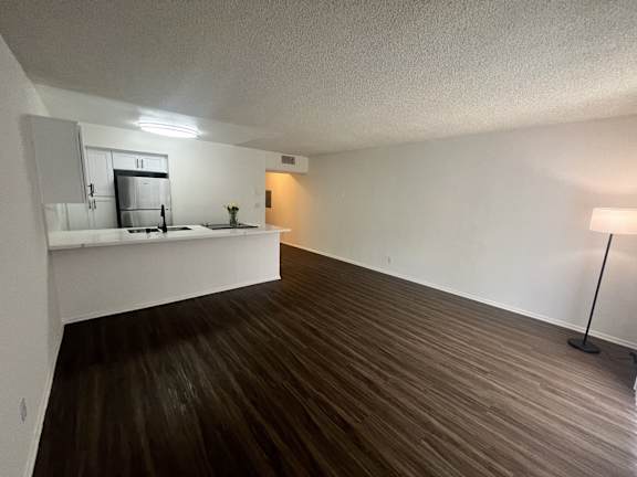 an empty living room with wood flooring and a kitchen