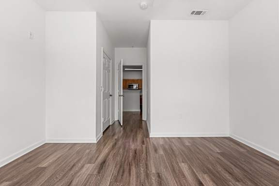 A room with white walls and wooden flooring with a doorway leading to another room.