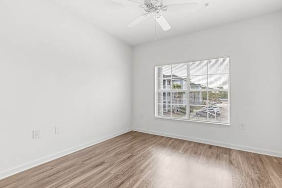 A room with a ceiling fan and a window showing a view of a house.