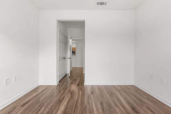 A room with white walls and wooden flooring with a doorway leading to another room.