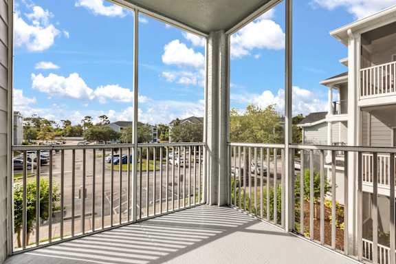 A balcony with a metal railing overlooks a parking lot and other buildings.