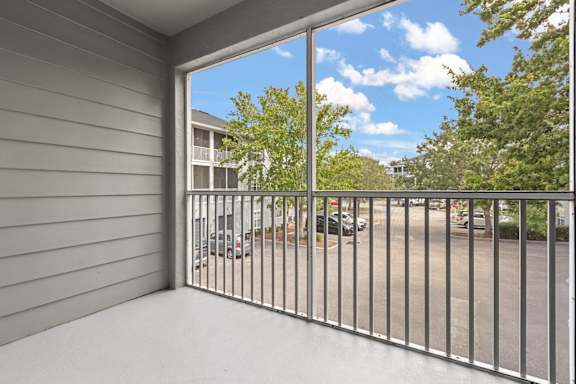 A balcony with a metal railing overlooks a parking lot.