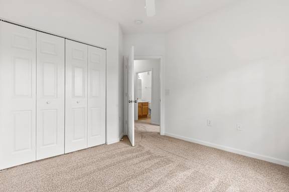 A room with white walls and carpeted floor with a door open to a hallway.