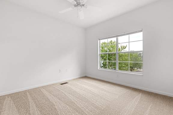 A room with a carpeted floor and a ceiling fan.