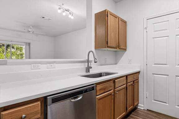 A kitchen with a stainless steel dishwasher and wooden cabinets.