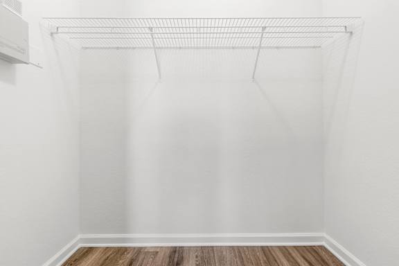 A white wall with a clothes rack and a wooden floor.
