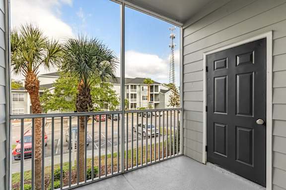 A balcony with a black door and a view of a parking lot and palm trees.