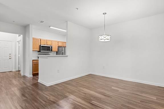 A room with wooden floors and a kitchen area in the background.