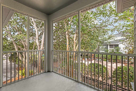 A balcony with a metal railing and a view of a street and trees.