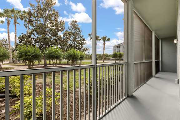 A balcony with a metal railing overlooks a green lawn and trees.