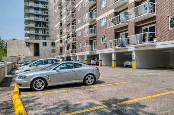 A silver car is parked in a parking lot next to a tall apartment building.