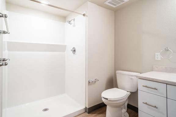 A white bathroom with a toilet, sink, and shower. at All Saints Apartments, DENVER, CO