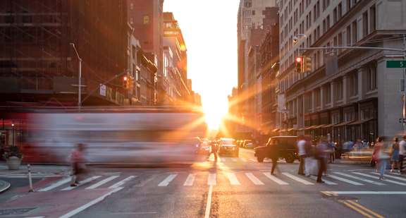 A busy city street at sunset with people crossing the road.