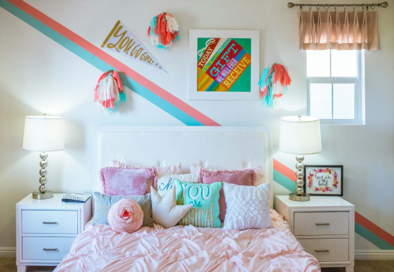 a bedroom with a bed with pink pillows and a rainbow wall