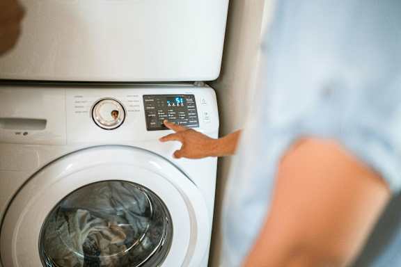 A person is pressing the start button on a washing machine.